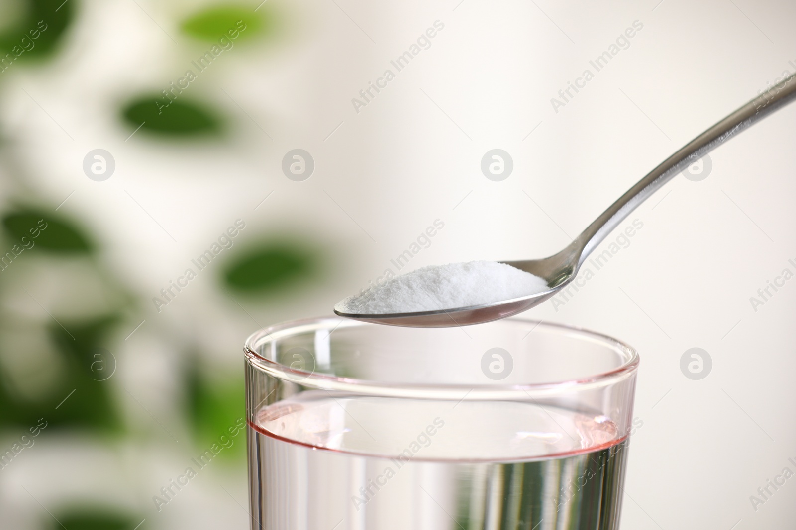 Photo of Spoon with baking soda over glass of water on blurred background, closeup