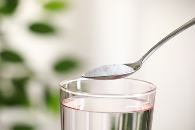 Spoon with baking soda over glass of water on blurred background, closeup