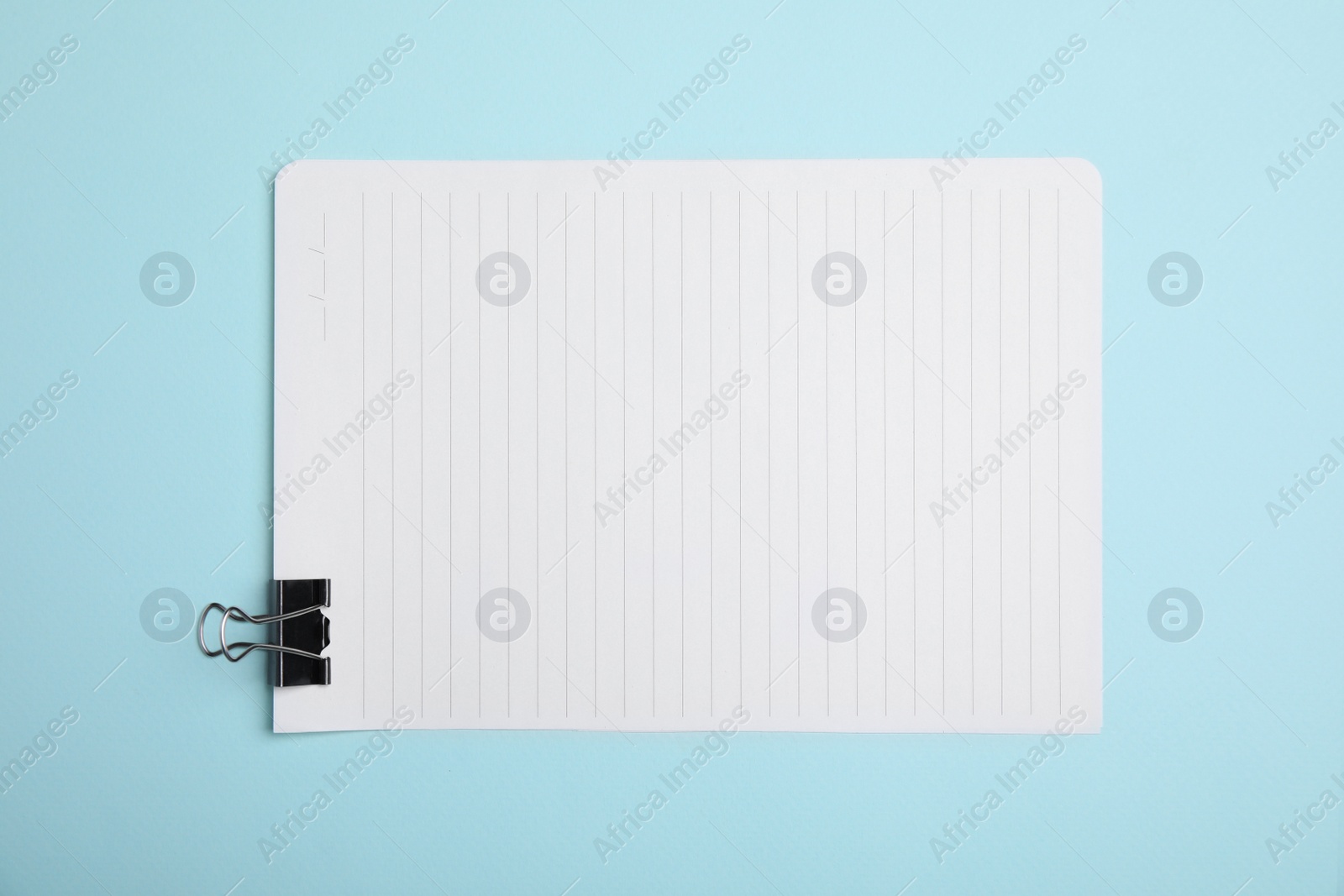 Photo of Sheet of paper with clip on light blue background, top view