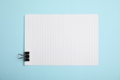 Photo of Sheet of paper with clip on light blue background, top view