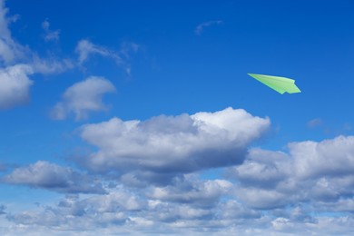 Image of Green paper plane flying in blue sky with clouds