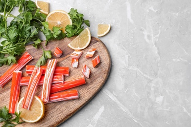 Photo of Delicious crab sticks with parsley and lemon on light grey marble table, flat lay. Space for text