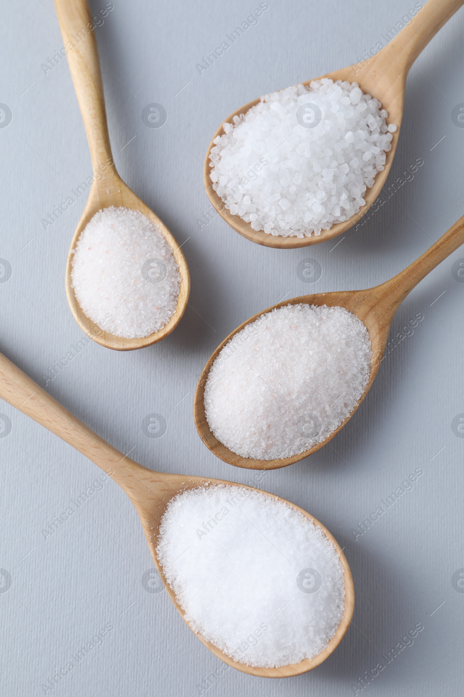 Photo of Organic white salt in spoons on light grey background, flat lay