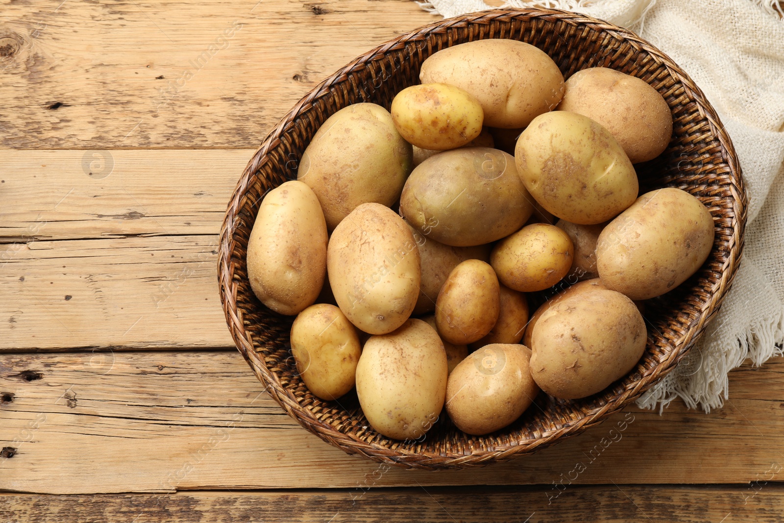 Photo of Raw fresh potatoes in wicker basket on wooden table, top view. Space for text