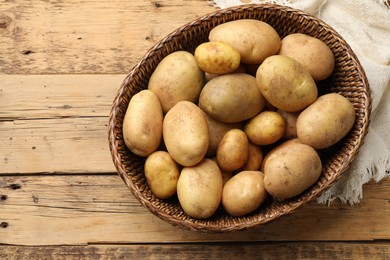 Photo of Raw fresh potatoes in wicker basket on wooden table, top view. Space for text