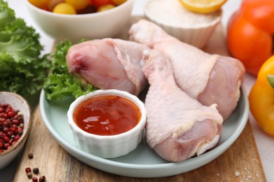 Fresh marinade, raw chicken drumsticks and lettuce on table, closeup