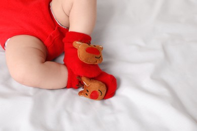 Baby wearing festive Christmas socks on white bedsheet, closeup. Space for text