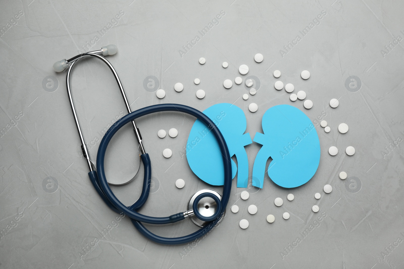 Photo of Paper cutout of kidneys, stethoscope and pills on grey table, flat lay