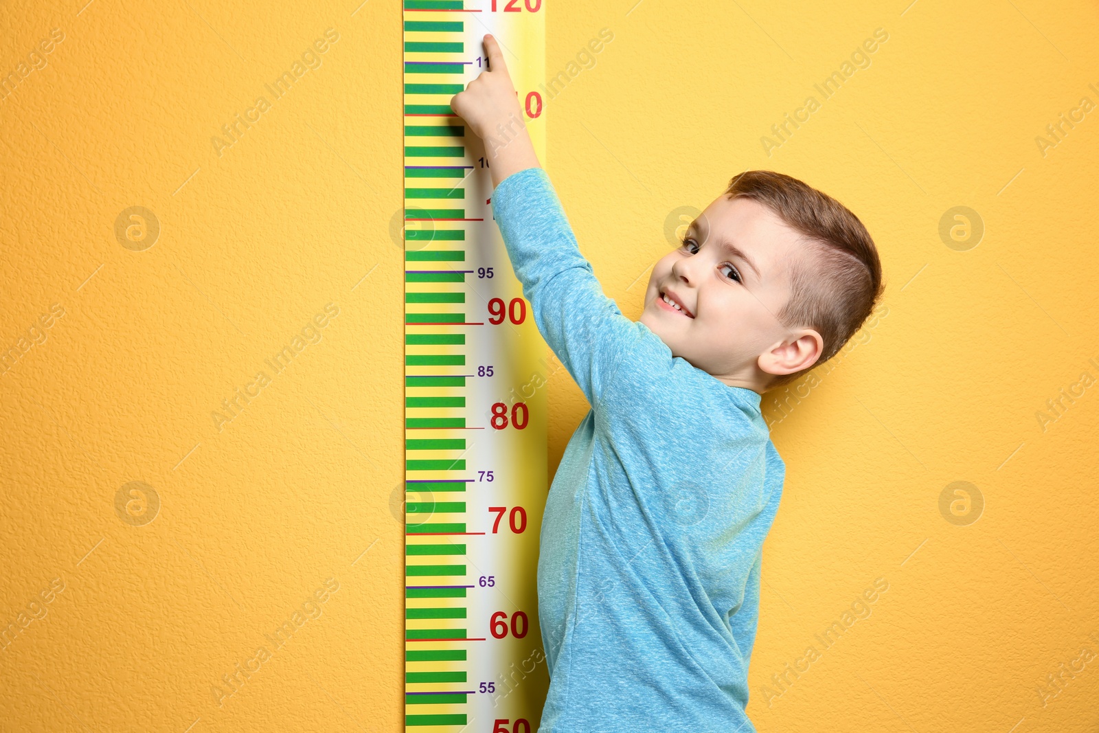 Photo of Little boy measuring his height on color background