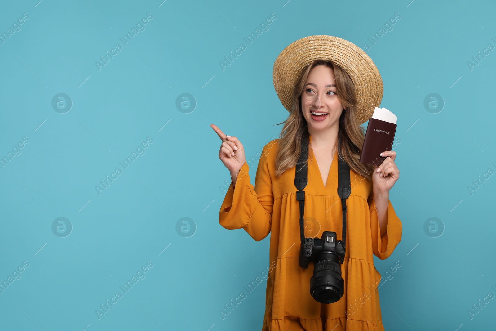 Photo of Happy young woman with camera, passport, ticket and hat pointing at something on light blue background, space for text