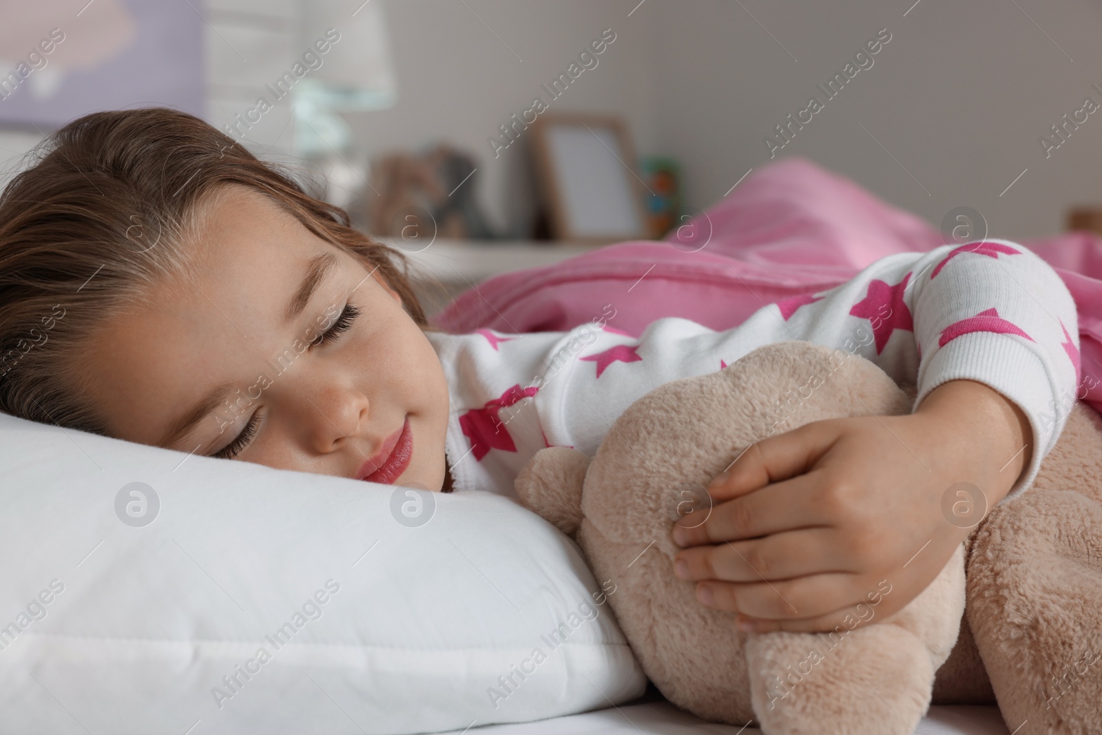 Photo of Cute little girl with toy bear sleeping in bed at home