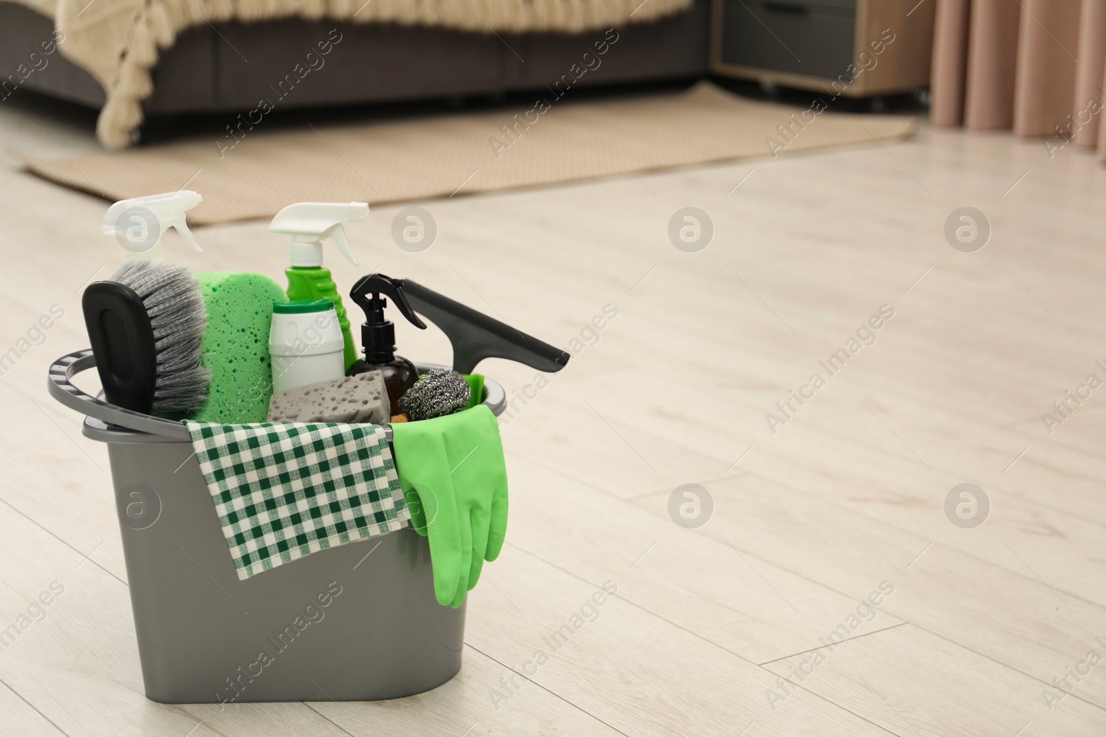 Photo of Different cleaning supplies in bucket on floor at home, space for text