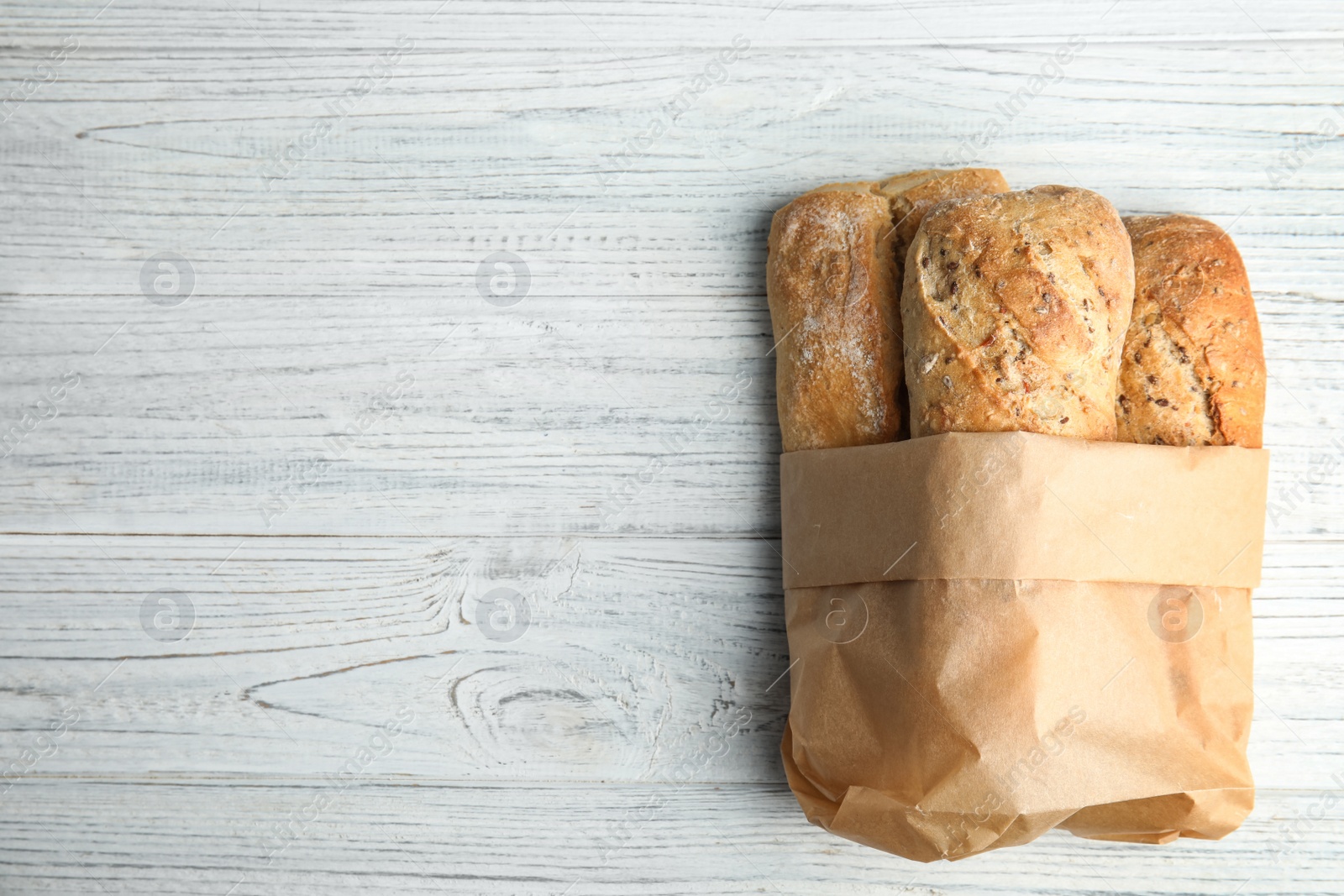 Photo of Mini baguettes in paper bag on wooden table, top view with space for text. Wholegrain bread