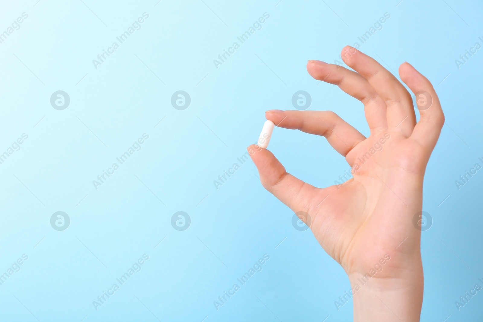 Photo of Woman holding vitamin capsule on light blue background, closeup. Space for text