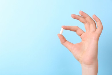 Woman holding vitamin capsule on light blue background, closeup. Space for text