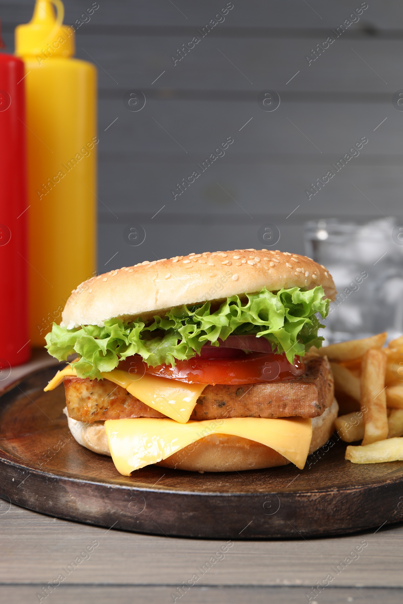 Photo of Delicious tofu burger served with french fries on grey wooden table