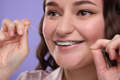 Photo of Woman with braces cleaning teeth using dental floss on violet background, closeup