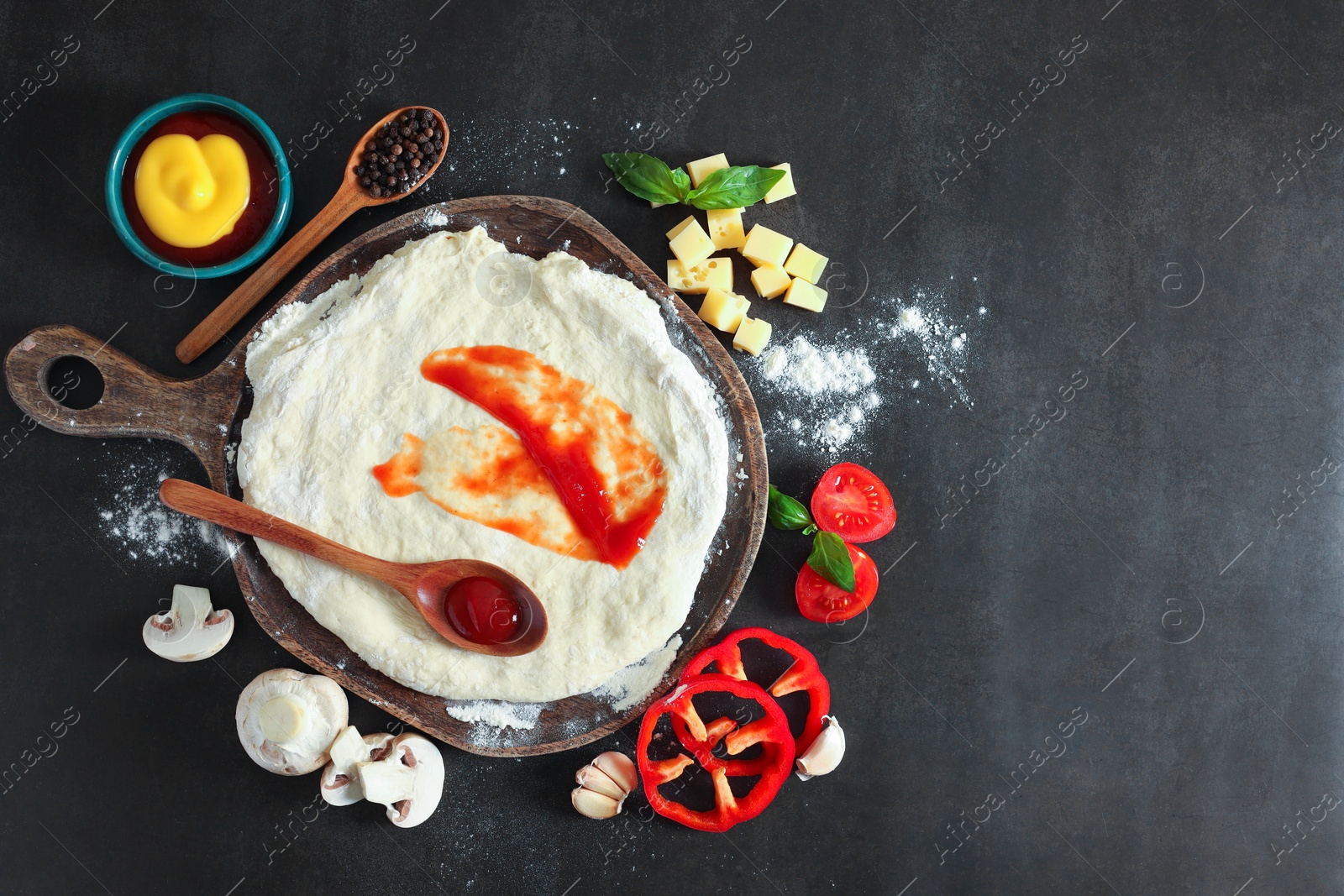 Photo of Pizza dough with tomato sauce and products on dark table, flat lay. Space for text
