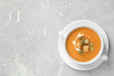 Photo of Tasty creamy pumpkin soup with croutons, seeds and dill in bowl on light grey table, top view. Space for text