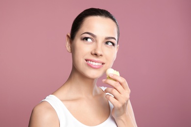 Young woman applying balm on her lips against color background