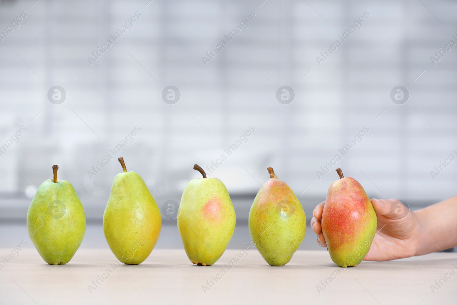 Photo of Woman taking fresh ripe pear from table in kitchen, closeup. Space for text