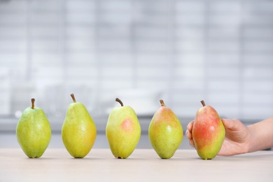 Woman taking fresh ripe pear from table in kitchen, closeup. Space for text