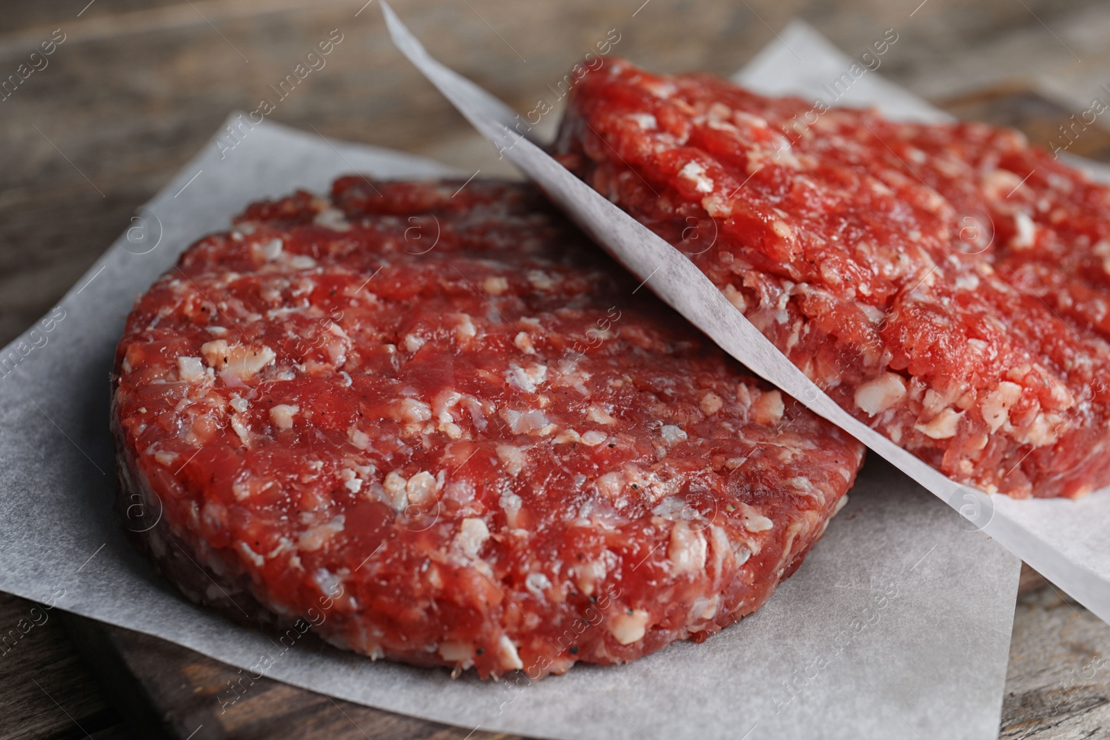 Photo of Raw meat cutlets for burger on wooden board, closeup
