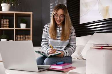 Young woman writing down notes during webinar at home