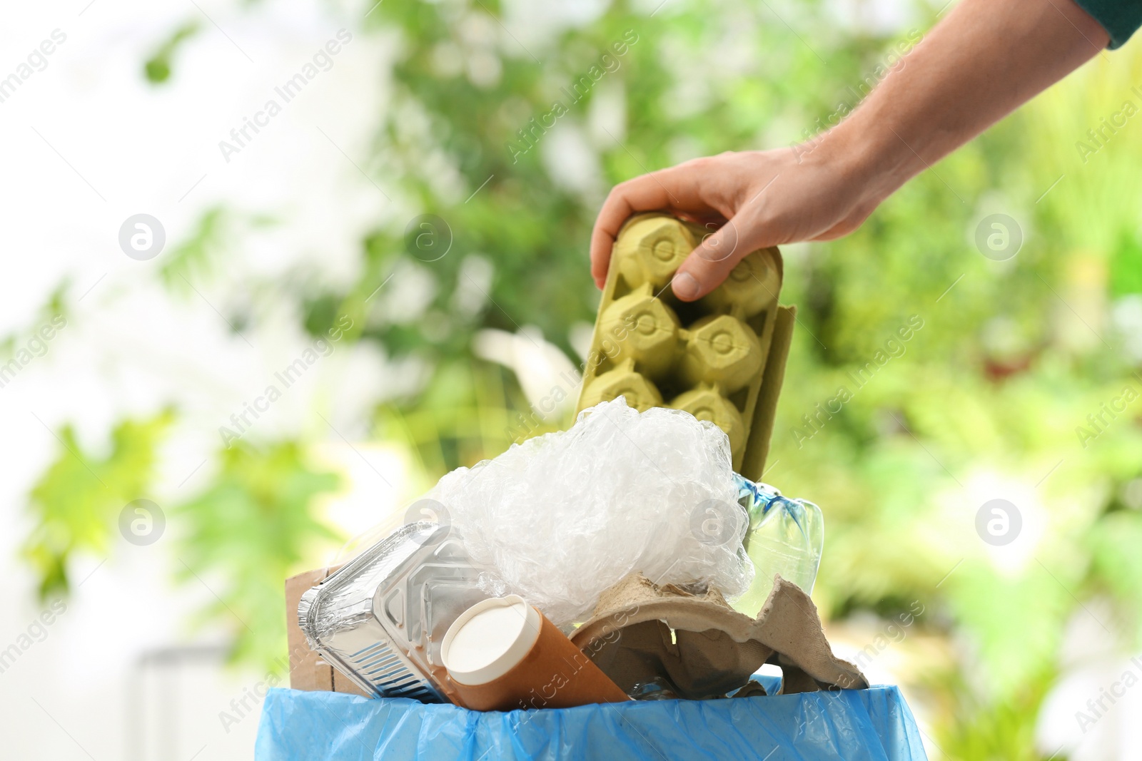 Photo of Man putting paper garbage into trash bin on blurred background, closeup with space for text. Recycling problem