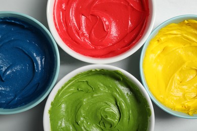 Photo of Bowls of different cream with food coloring on white marble table, flat lay