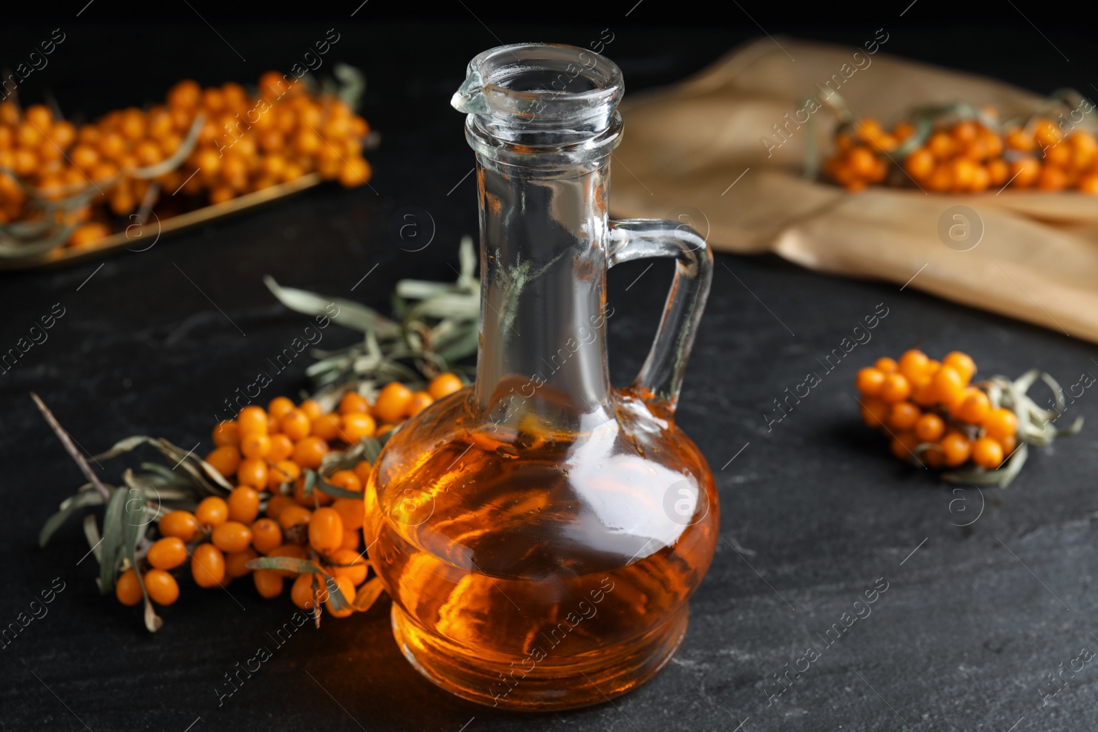 Photo of Ripe sea buckthorn and jug of essential oil on black table