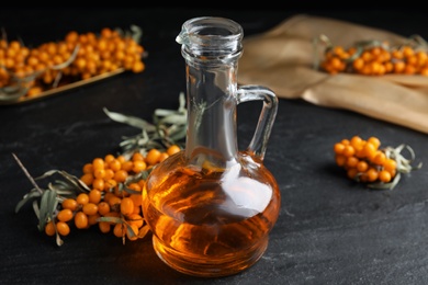 Photo of Ripe sea buckthorn and jug of essential oil on black table