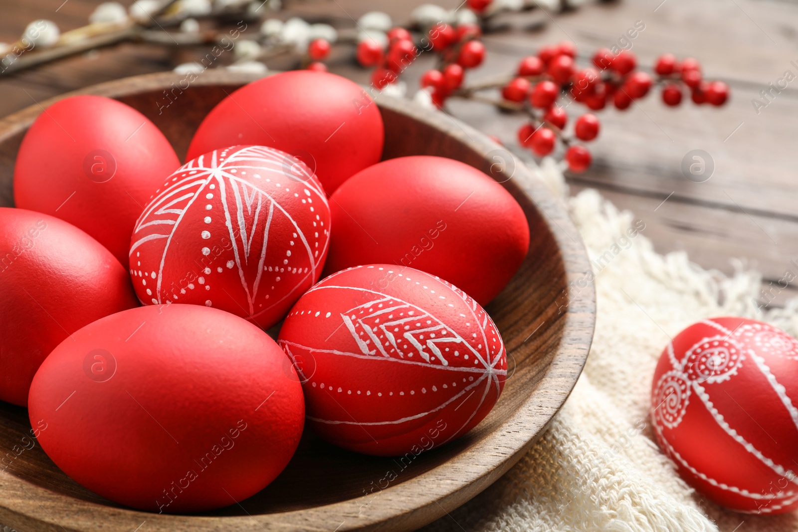 Photo of Wooden bowl with red painted Easter eggs on table, closeup