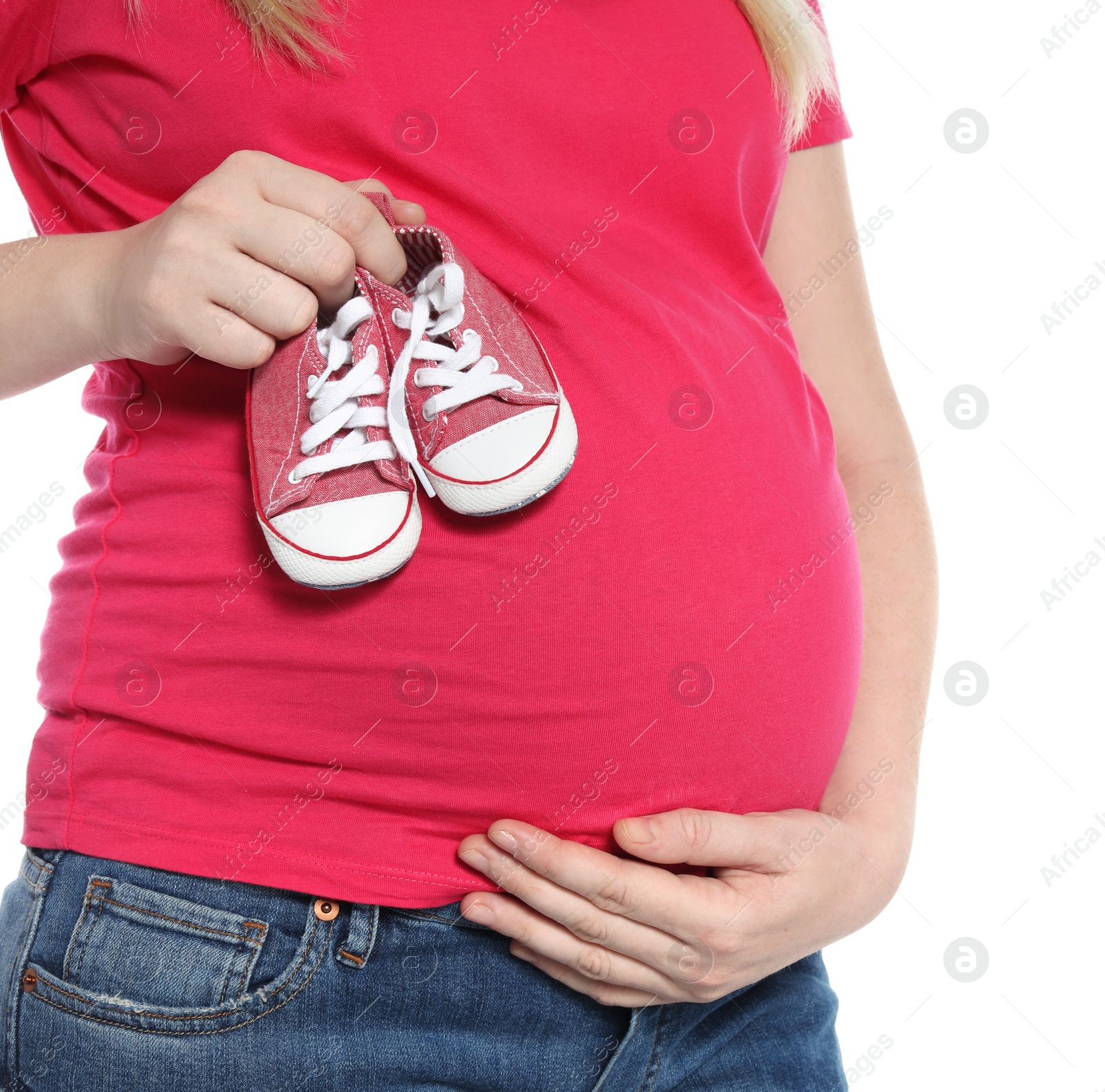 Photo of Pregnant woman holding baby booties near tummy on white background