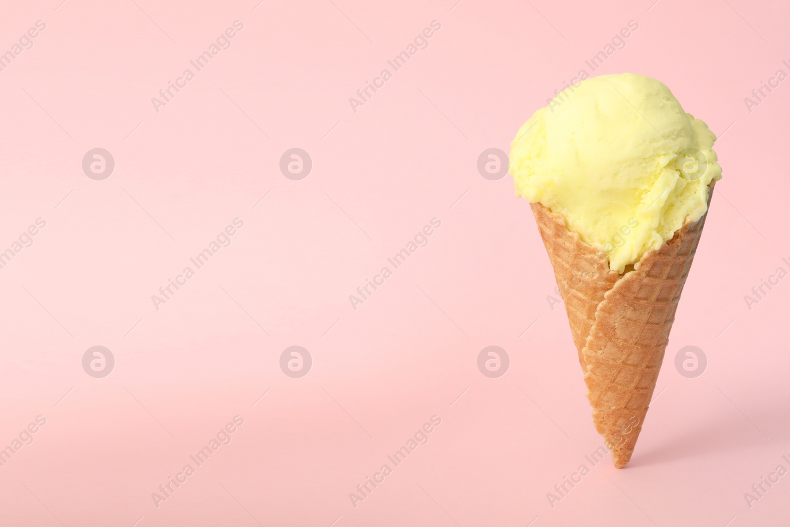 Photo of Delicious yellow ice cream in waffle cone on pink background. Space for text