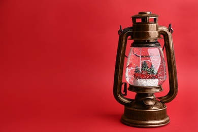 Photo of Beautiful snow globe in vintage lantern on red background, space for text