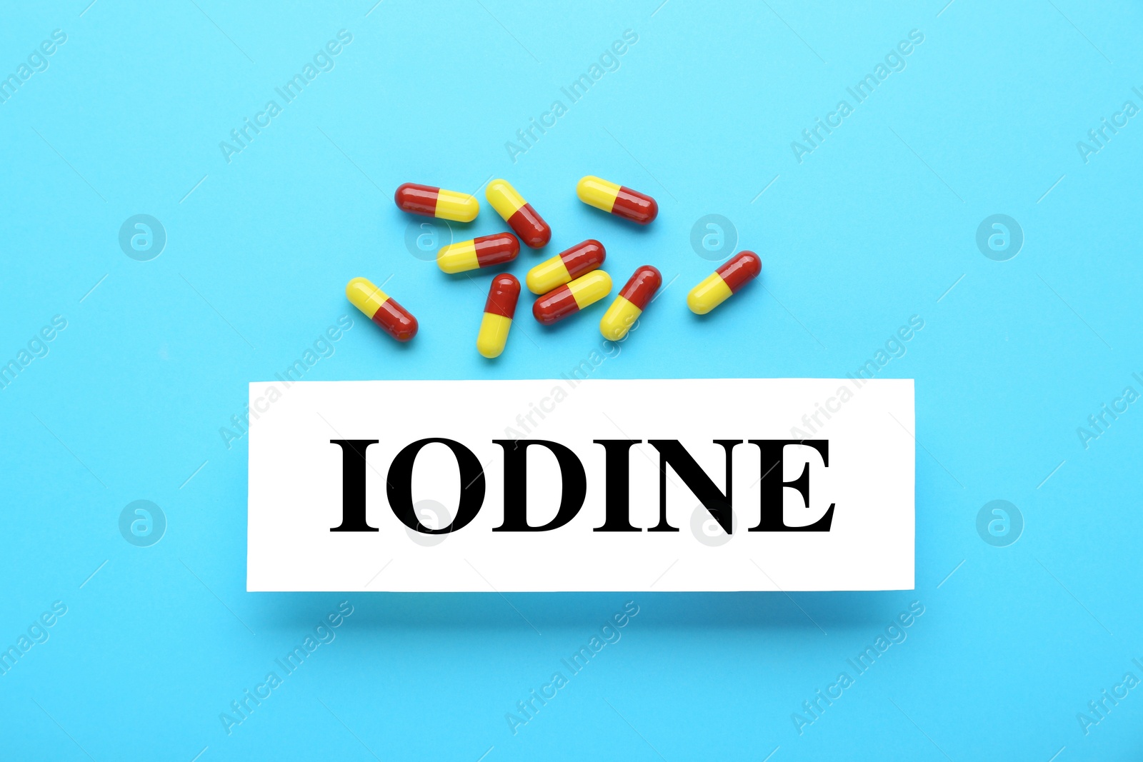 Photo of Card with word Iodine and pills on light blue background, flat lay