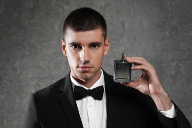 Photo of Handsome young man with bottle of perfume on grey stone background