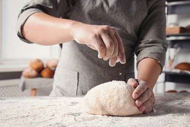 Man sprinkling flour over dough at table in kitchen, closeup