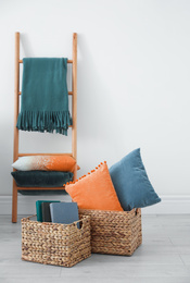Blue and orange pillows in wicker basket near decorative ladder indoors 