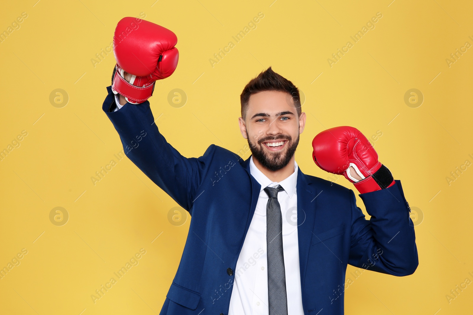 Photo of Happy young businessman with boxing gloves celebrating victory on color background