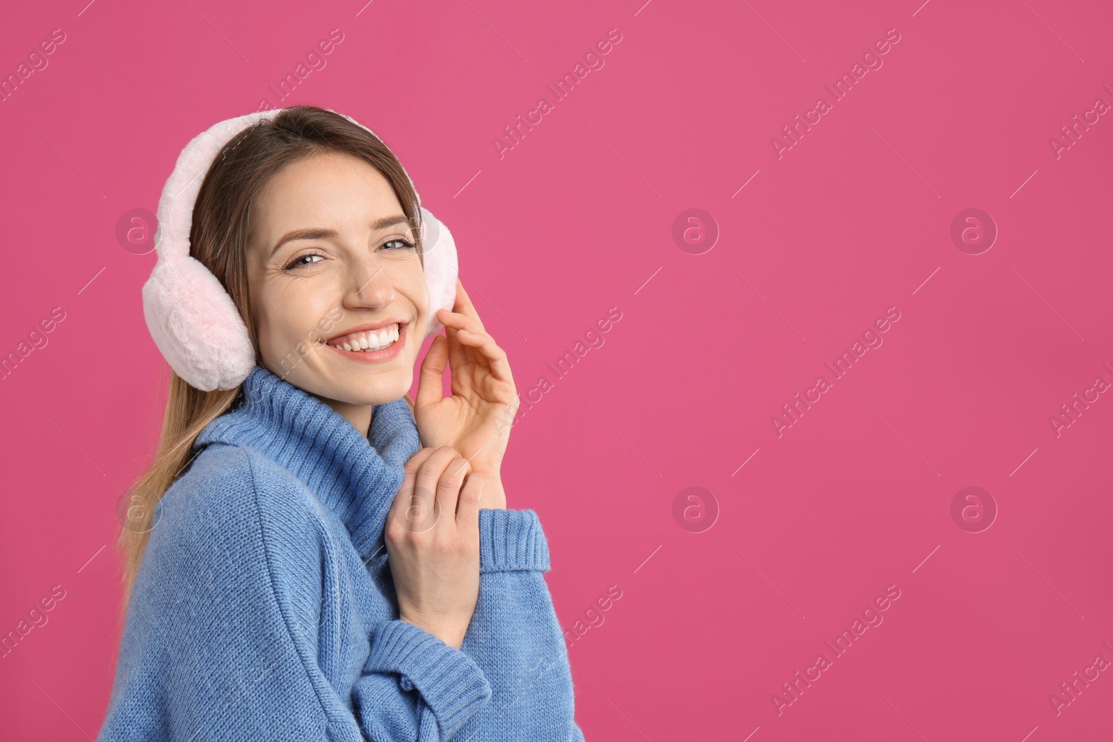 Photo of Happy woman wearing warm earmuffs on pink background, space for text