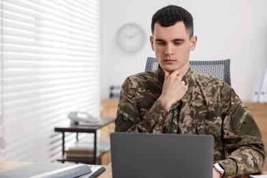 Photo of Military service. Young soldier working with laptop at table in office