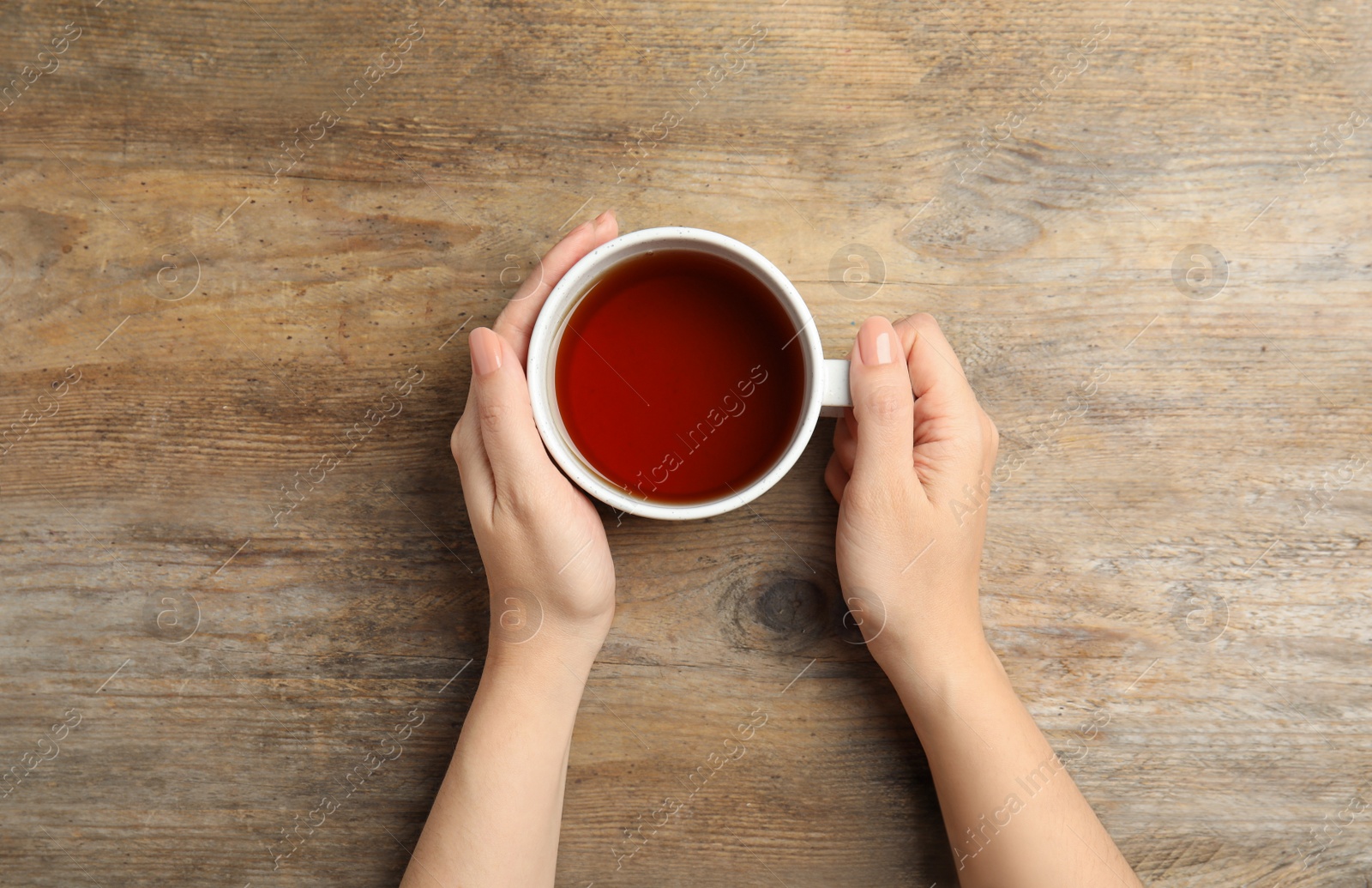 Photo of Woman with cup of tea at wooden table, top view