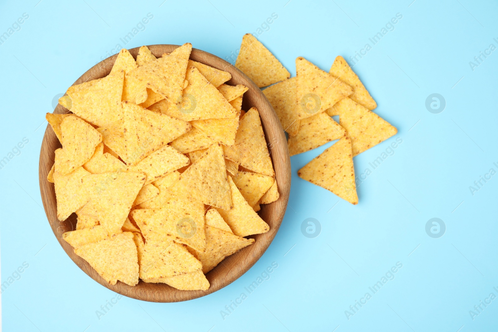 Photo of Wooden bowl of tasty Mexican nachos chips on light blue background, top view