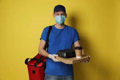 Courier in protective mask and gloves holding order on yellow background. Food delivery service during coronavirus quarantine