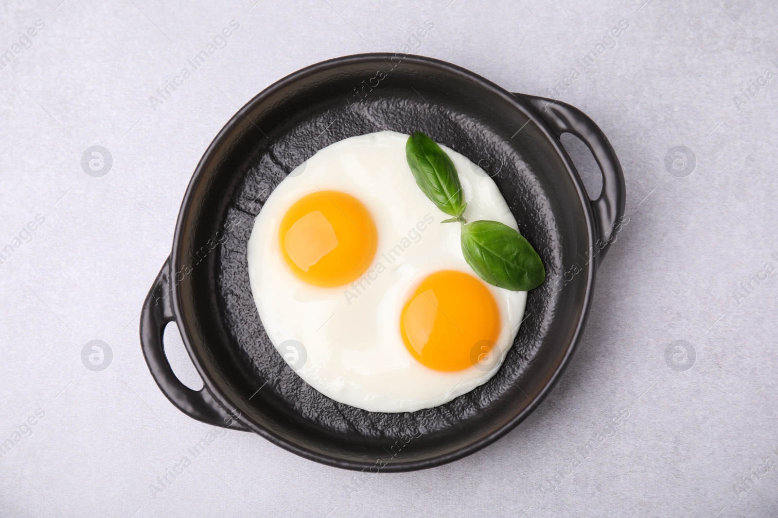 Photo of Tasty fried eggs with basil in pan on white table, top view