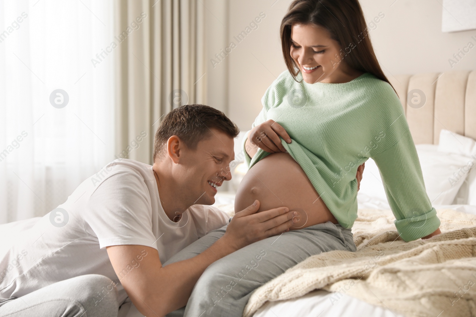 Photo of Young pregnant woman with her husband in bedroom