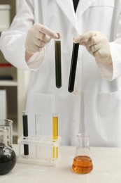 Photo of Laboratory worker holding test tubes with crude oil at light marble table, closeup