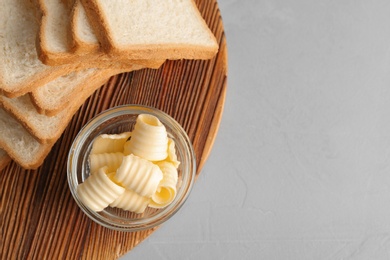 Photo of Bread with fresh butter curls on wooden board, top view